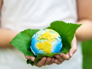 kid-holding-small-planet-in-hands-against-spring-or-summer-green-background-ecology-environment
