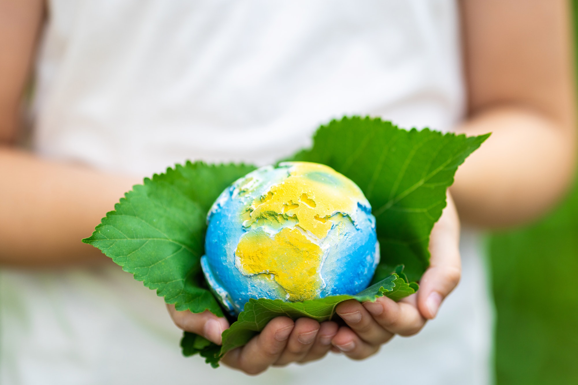 kid-holding-small-planet-in-hands-against-spring-or-summer-green-background-ecology-environment